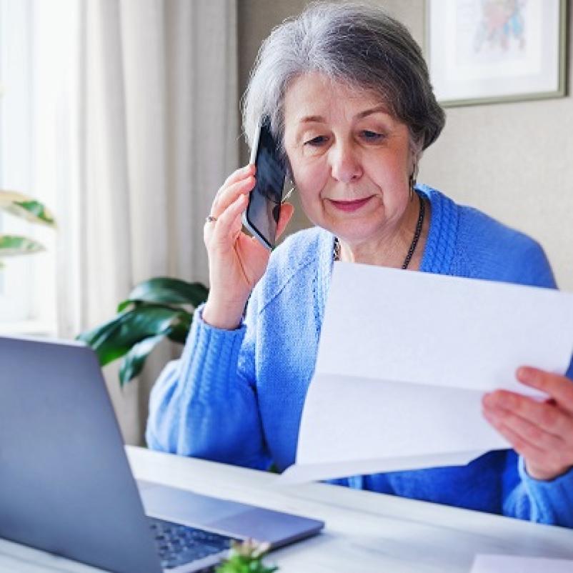 Vrouw bekijkt papieren met telefoon en laptop